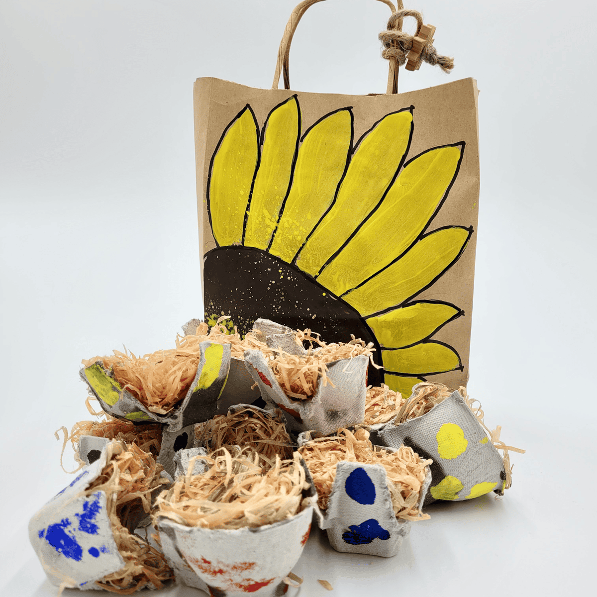 Anzündhilfe Feuerball: Eine dekorative Papiertüte im Sonnenblumendesign mit handgefertigten Saatgutstartern in bemalten, mit Stroh gefüllten Eierkartons.