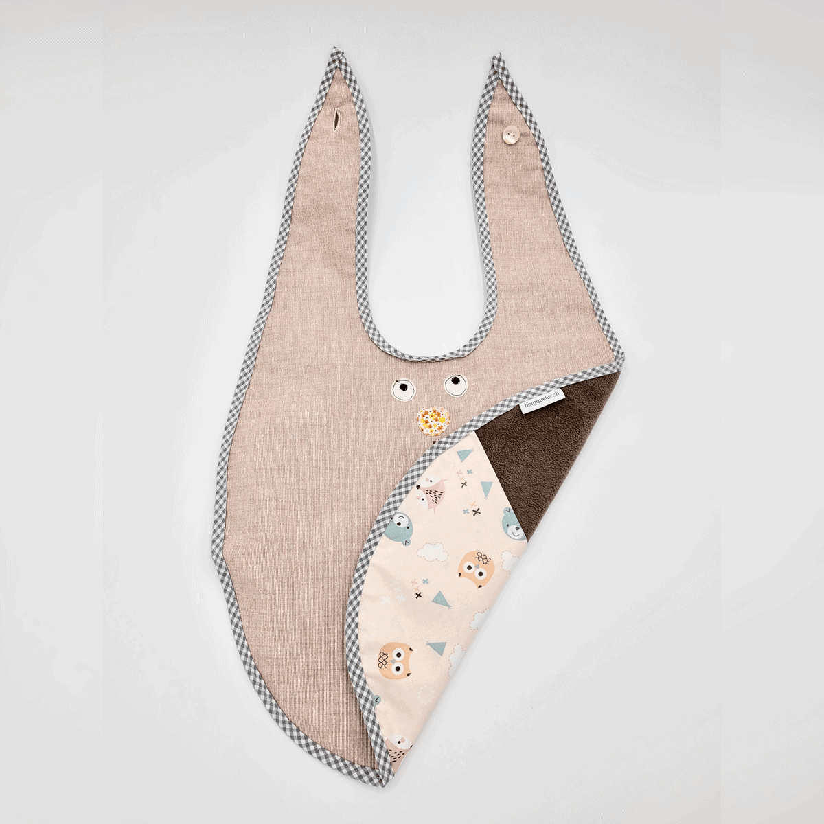 Das Esslätzchen ist ein graues Babylätzchen mit kariertem Rand und einem Eulenmuster, das auf der Innenseite dezent sichtbar ist.