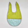 Ein Esslätzchen-Babylätzchen in Grün und Blau, in Hasenform mit kleinen Cartoon-Gesichtern und kariertem Rand.