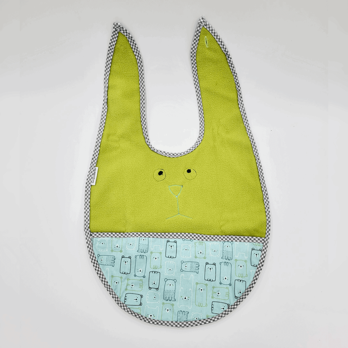 Ein Esslätzchen-Babylätzchen in Grün und Blau, in Hasenform mit kleinen Cartoon-Gesichtern und kariertem Rand.