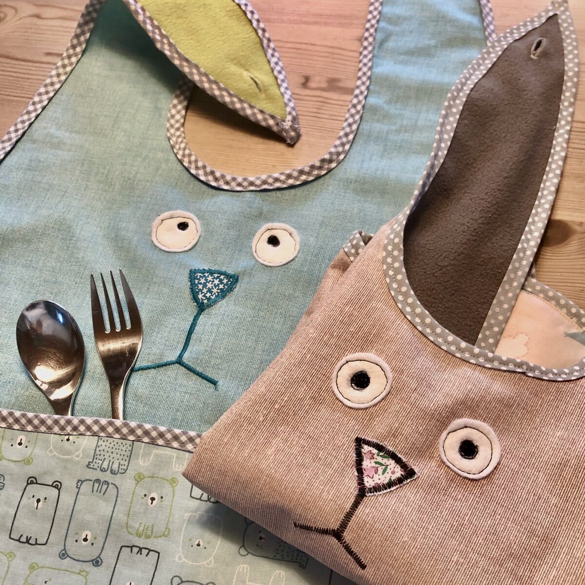 Esslätzchen mit Tiermotiven, Lätzchen und Besteck auf einem Holztisch ausgestellt.