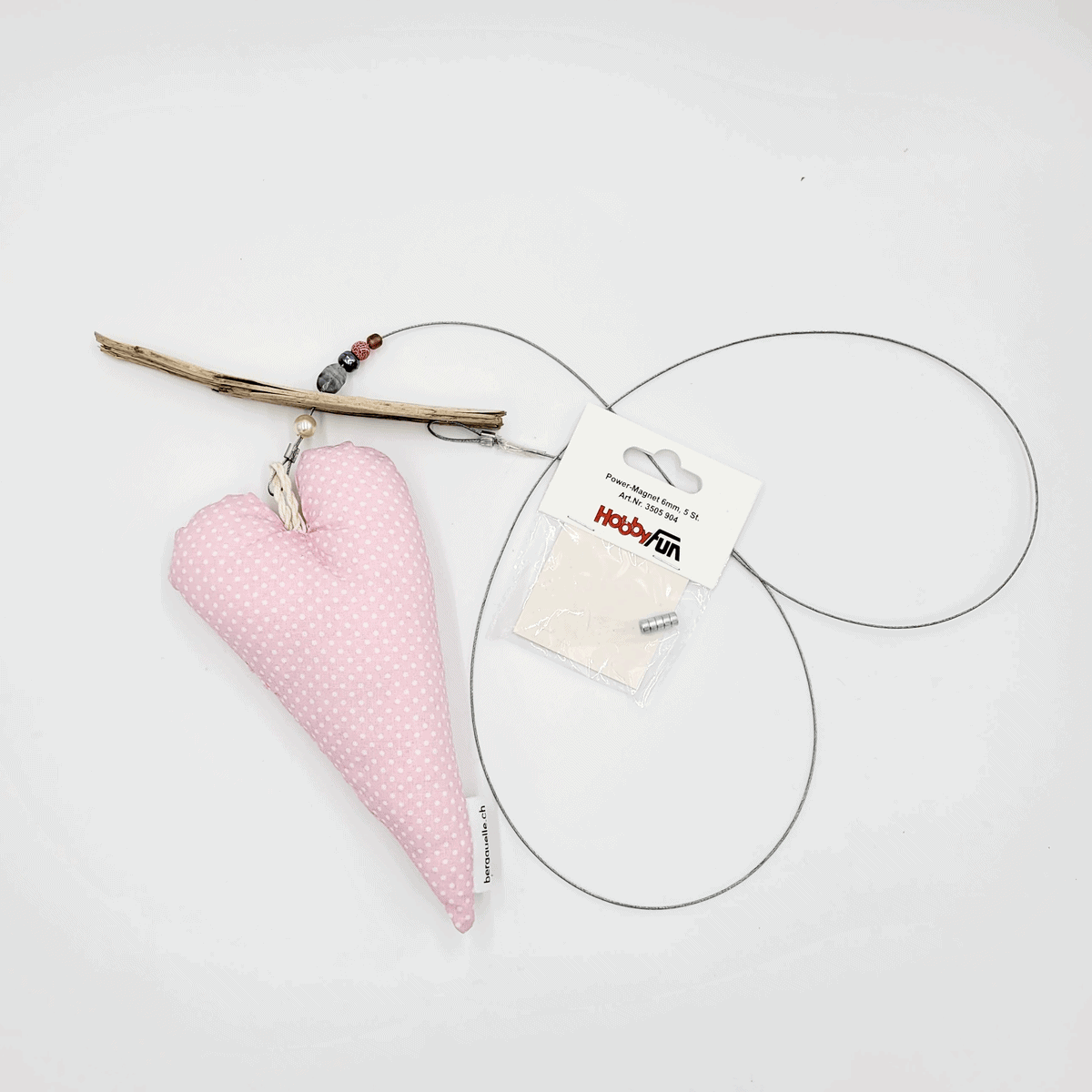 Die „Fotoleine mit Herz“ zeigt ein rosa gepunktetes Herzornament aus Treibholz und Draht, das neben einem Paket mit der Aufschrift „Happy Fun“ ruht.