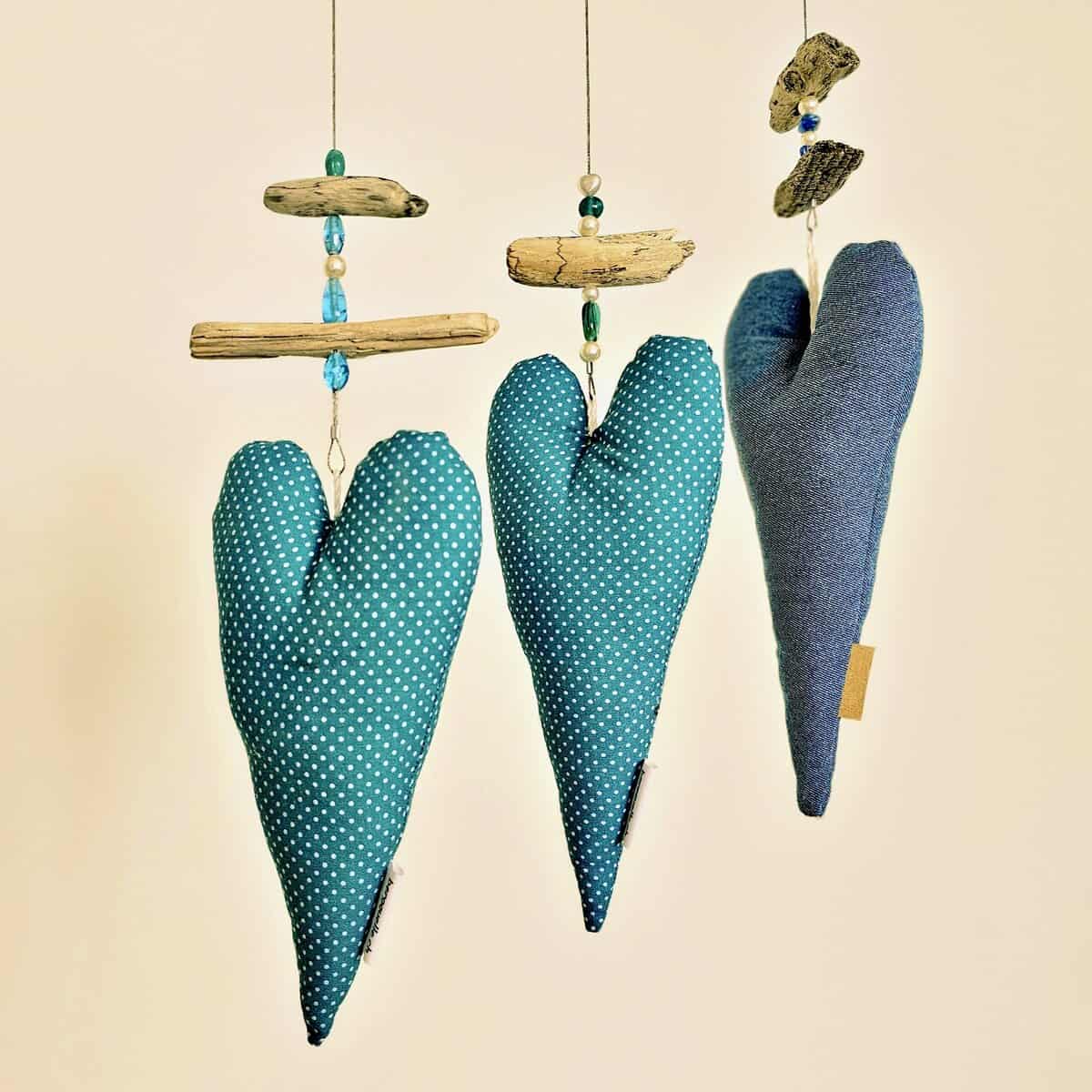 Die „Fotoleine mit Herz“ zeigt drei herzförmige Stoffdekorationen in Blau- und Grüntönen, geschmückt mit Treibholz und Perlen.