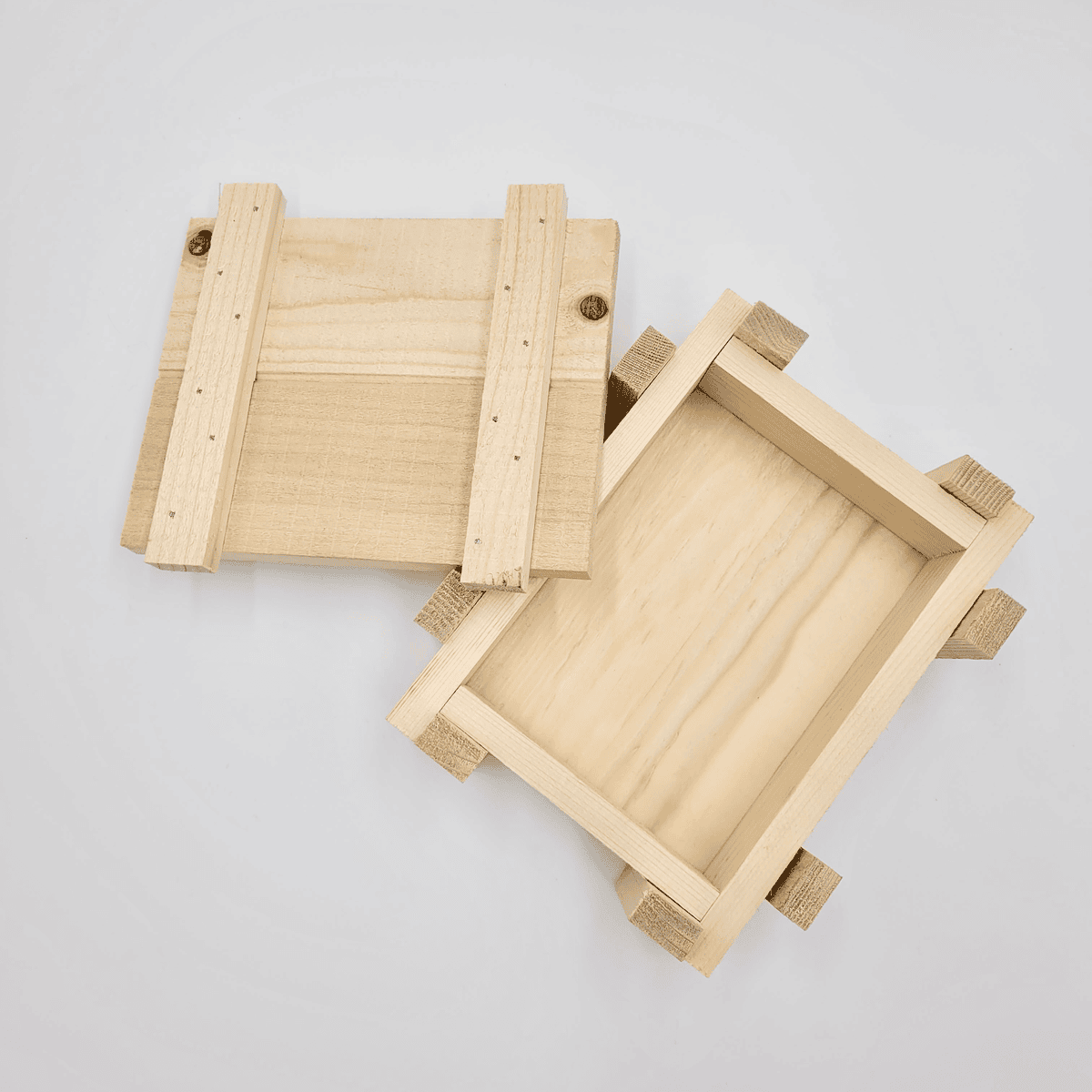 Zwei kleine Holzkisten auf weißem Hintergrund, wobei eine Kiste teilweise geöffnet und die andere obenauf gestapelt ist.