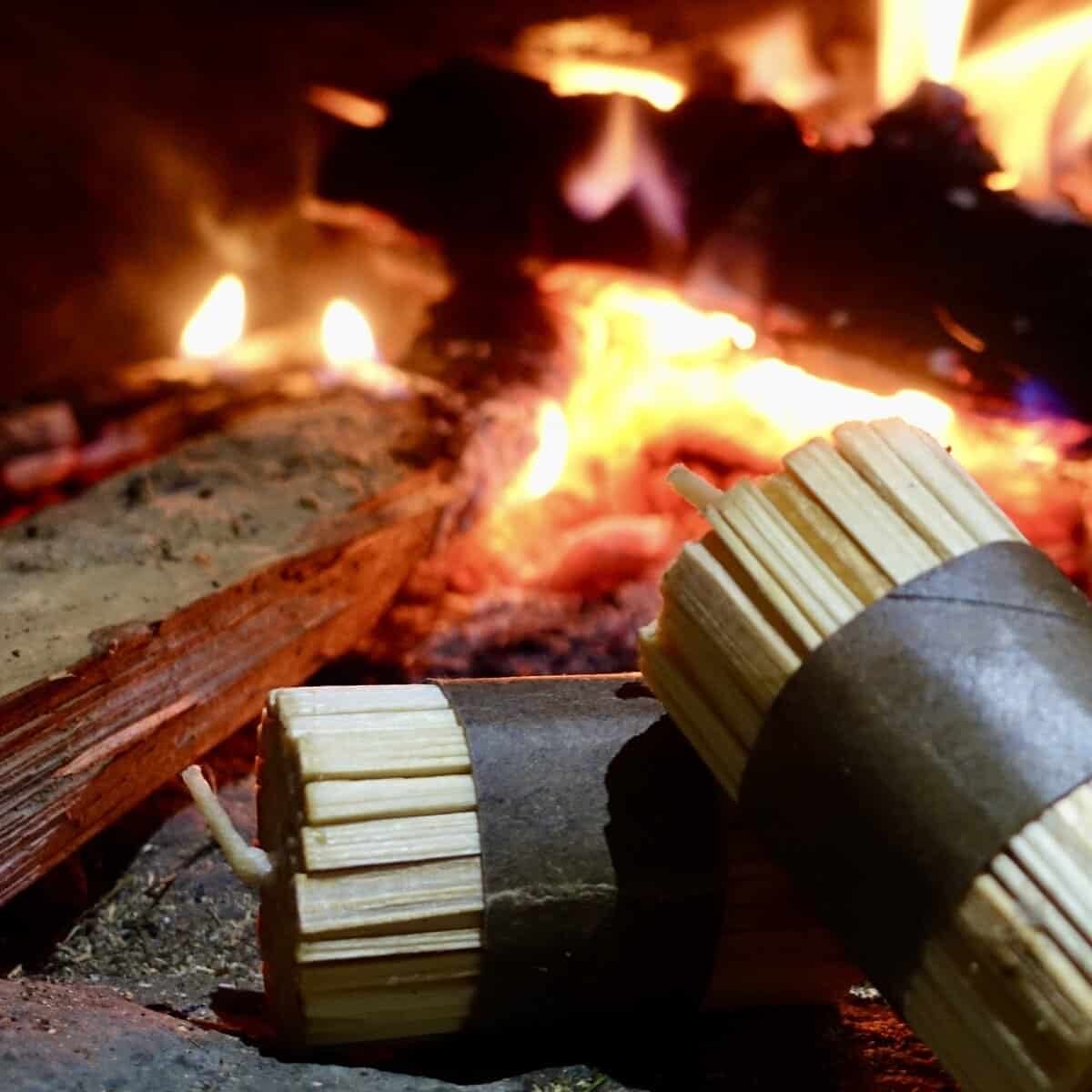 K-LUMET-Bündel aus Anzündhölzern, in Papier eingewickelt, neben einem warmen, brennenden Feuer.