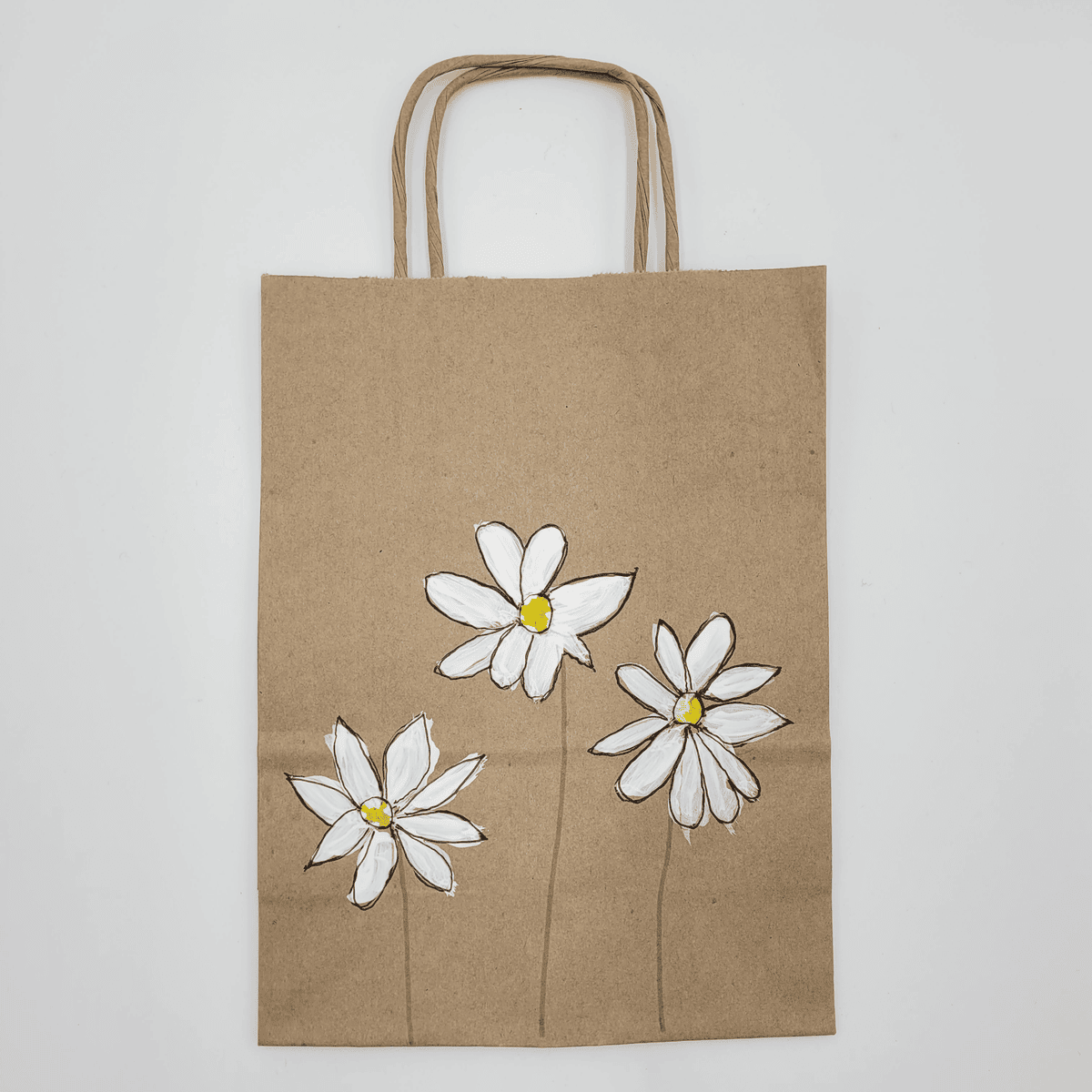 Braune Papiertüte namens „Papiertasche bemalt“ mit drei weißen Gänseblümchen darauf.