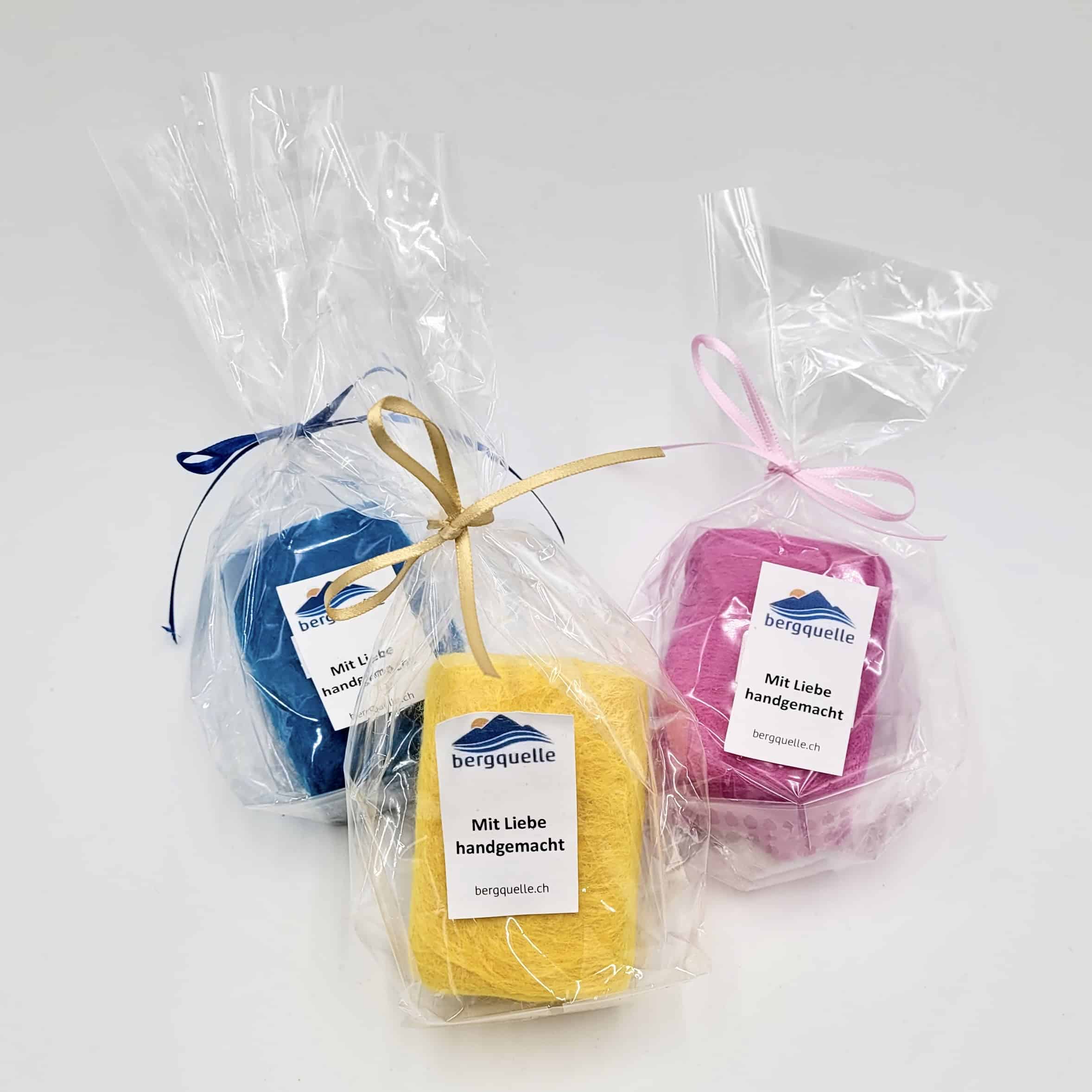 Drei Riegel Schafmilchseife in Klarsichtfolie verpackt, jeweils mit einer farbigen Schleife zusammengebunden und mit der Aufschrift „Mit Liebe handgemacht“ versehen.