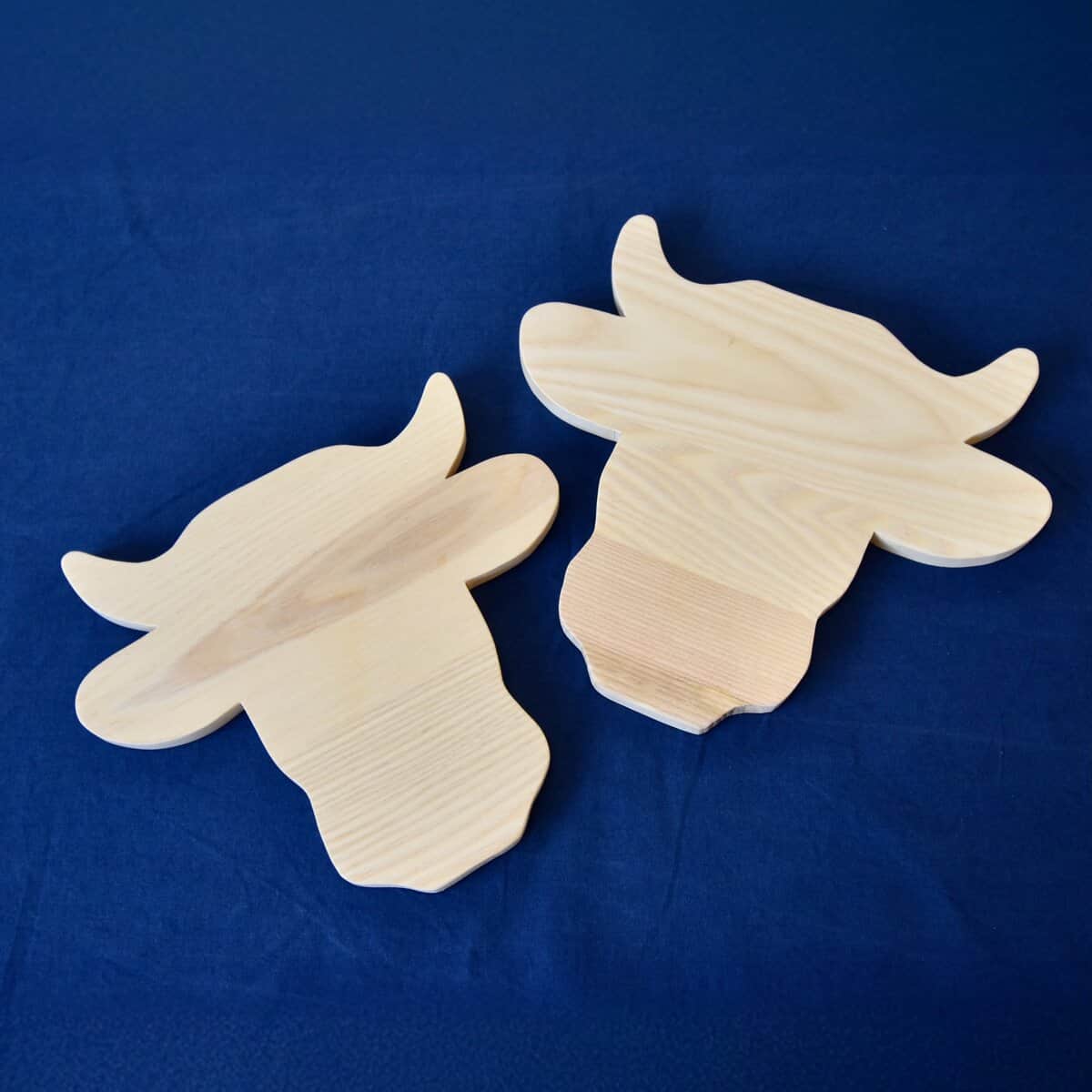Auf einem dunkelblauen Hintergrund ruhen zwei Holzausschnitte vom Typ „Schneidebrett Kuh“.
