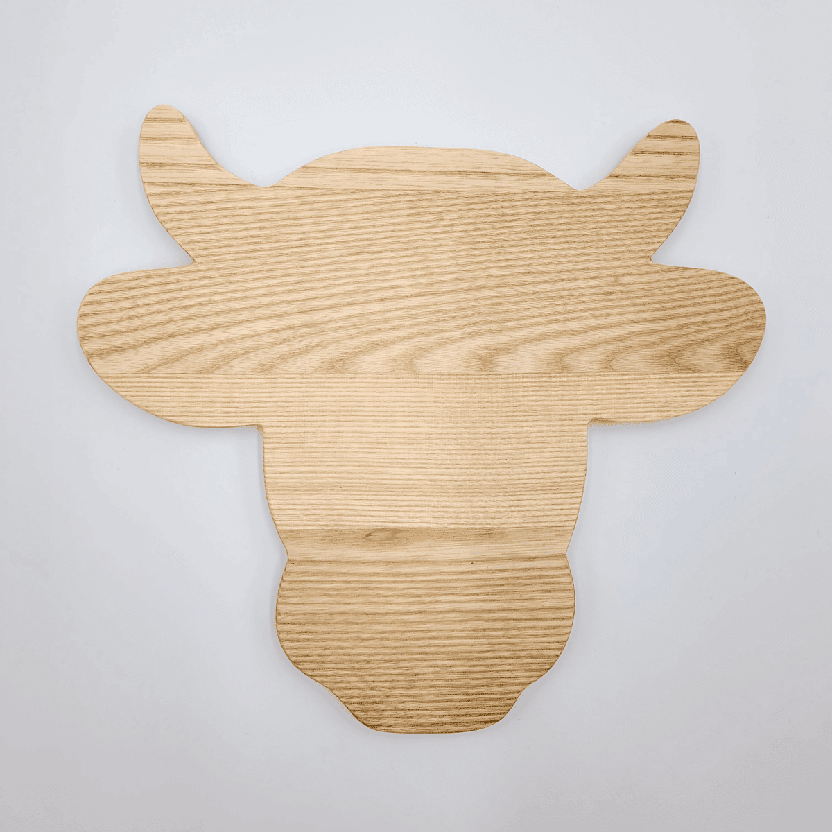 Das „Schneidebrett Kuh“ ist ein hölzernes Schneidebrett in Form eines Kuhkopfes auf grauem Untergrund.