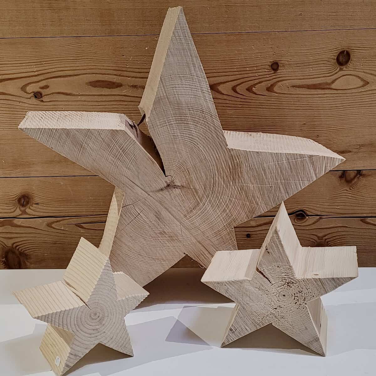 Drei hölzerne Sternskulpturen in verschiedenen Größen vor einem Hintergrund aus Holzbrettern.