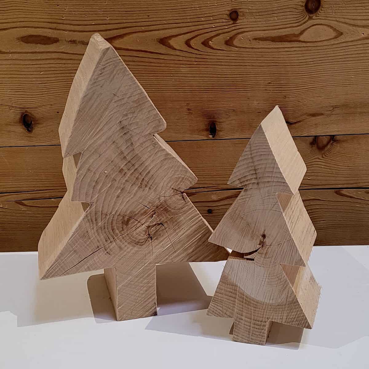 Die Tanne besteht aus zwei hölzernen Weihnachtsbaumskulpturen auf einer weißen Oberfläche, die vor einem hölzernen Wandhintergrund positioniert sind.