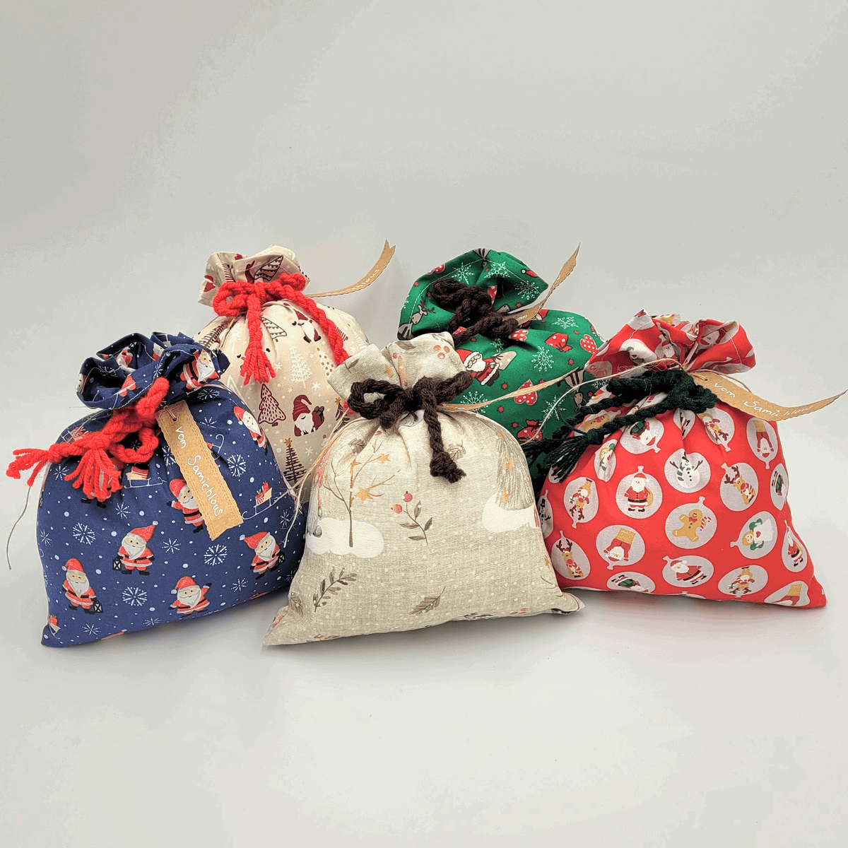 Fünf farbenfrohe Geschenktüten mit festlichen Mustern und Zugbändern, angeordnet auf einem einfarbigen Hintergrund.