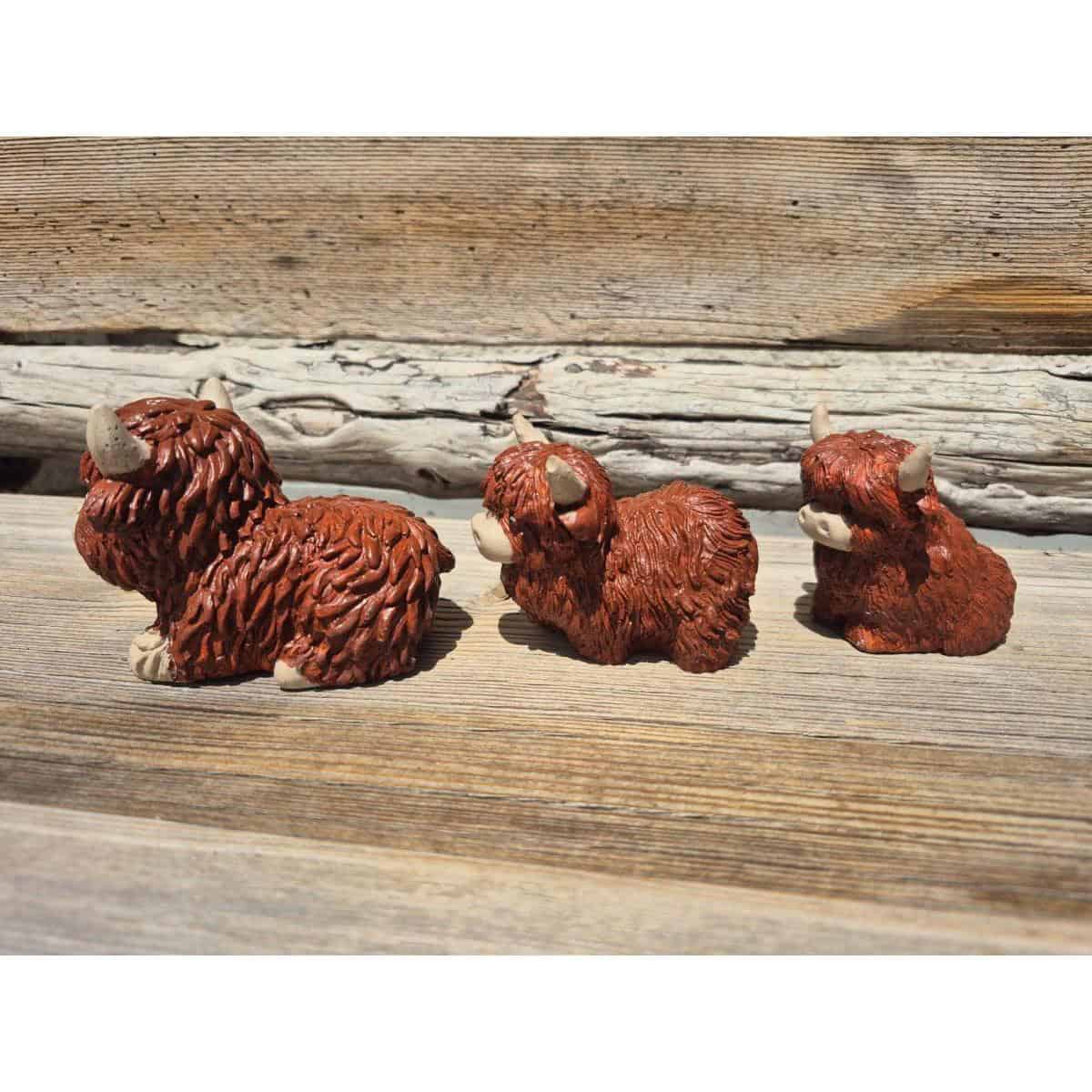 Drei kleine, braune Spüllappen-Figuren (Kopie) mit zotteligem Fell und Hörnern sitzen im Sonnenlicht auf verwitterten Holzplanken.